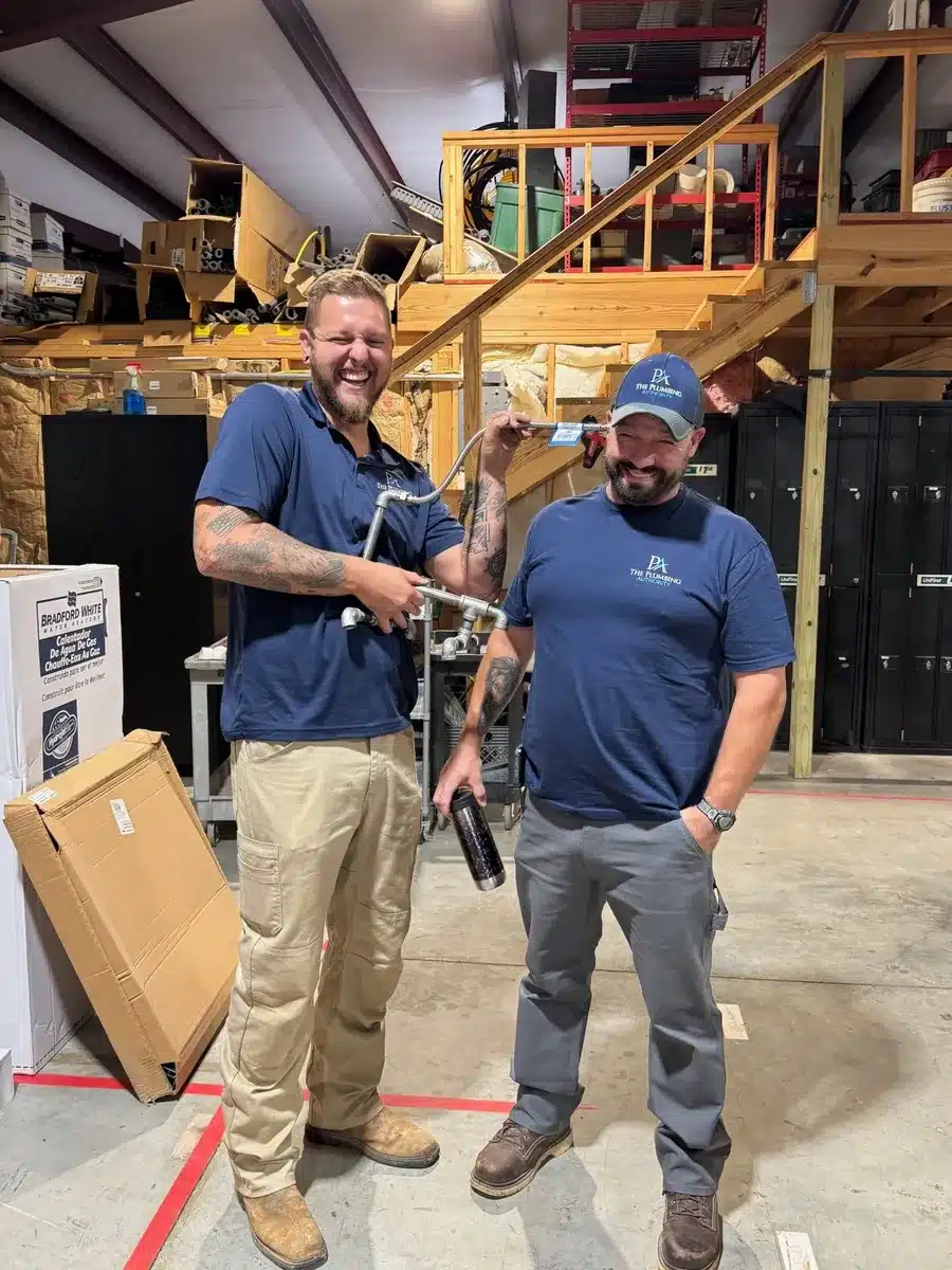 Two staff members posing with a pipe-assembly project for Winning Wednesday
